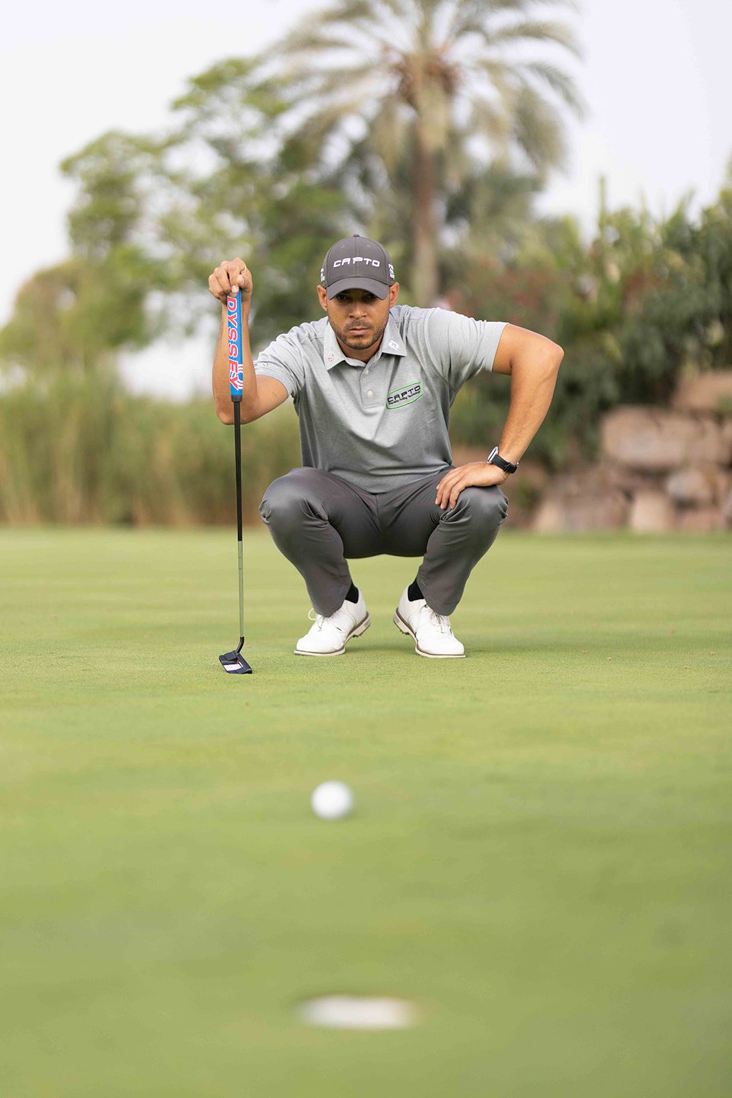 Golfeur accroupi derrière sa balle sur un green, putter en main, en train de lire la ligne